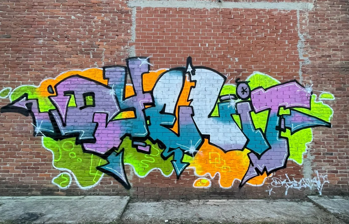 Graffito Dyelit su muro di mattoni, in viola, azzurro e verde lime.