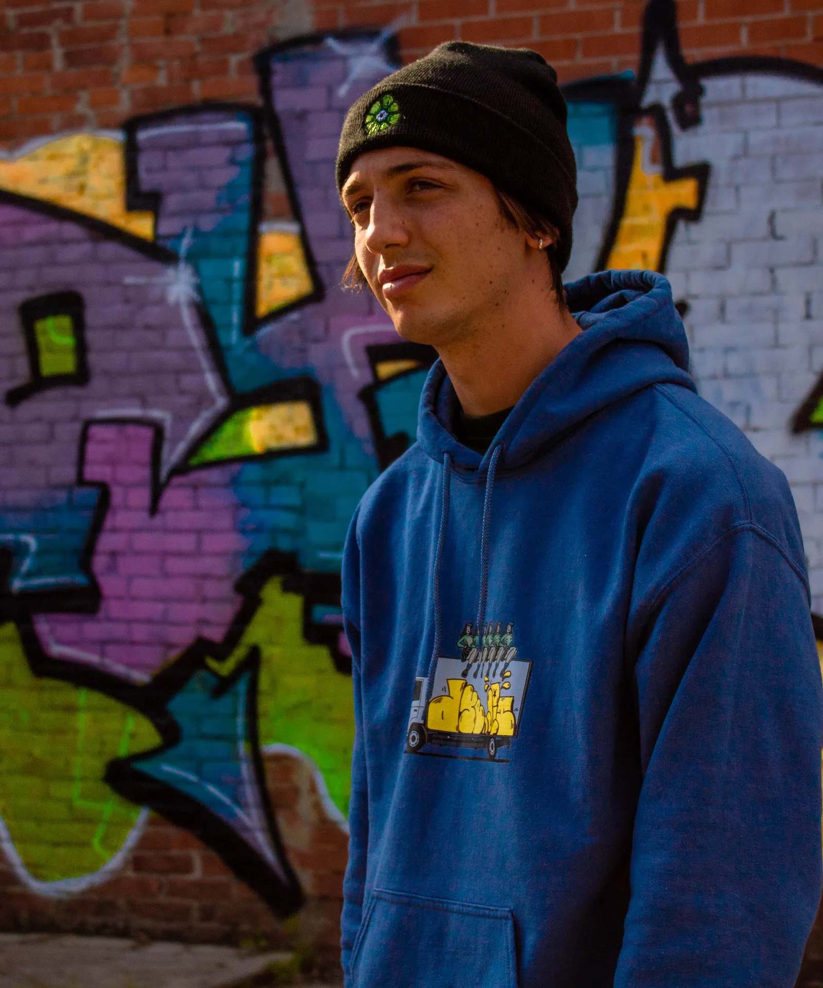 Un ragazzo con berretto e felpa blu Dyelit davanti al graffito.