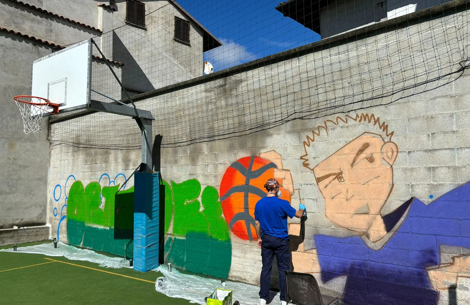 Il campetto da basket ripreso di lato, con il murales sulla parete di fondo.