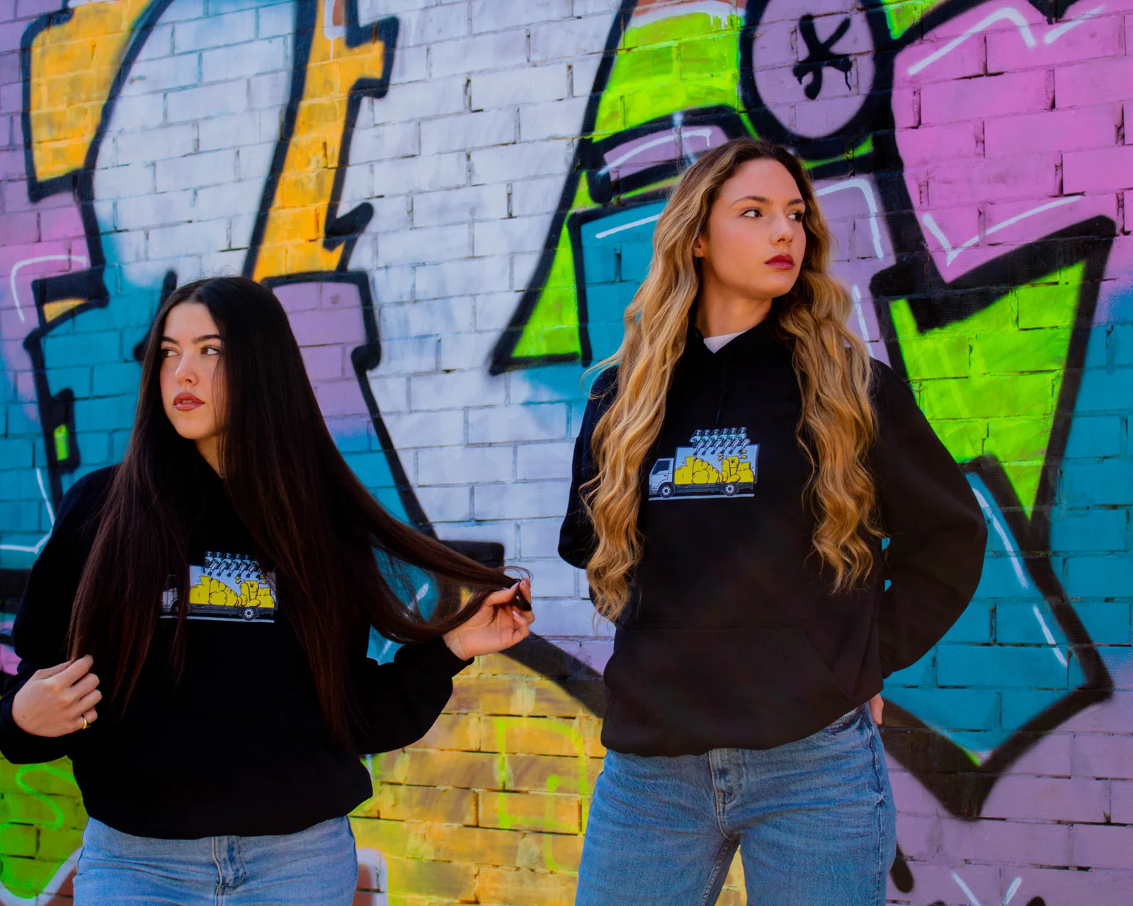 Due ragazze con la felpa Dyelit davanti al graffito.